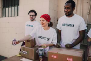 Three people with T-shirts on saying Volunteer handing out items from boxes